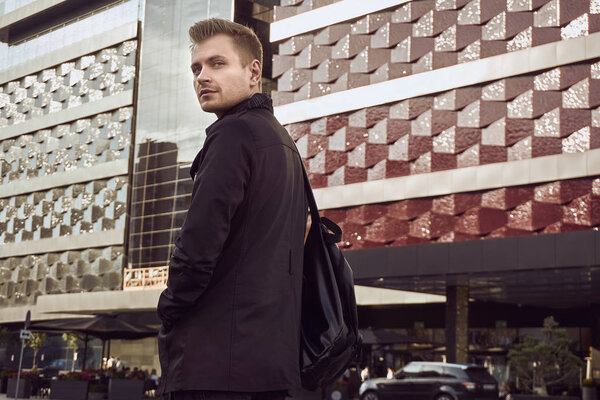 Портрет молодого красивого мужчины в тёмном пальто, смотрящего вдаль на сияющий на солнце фон
