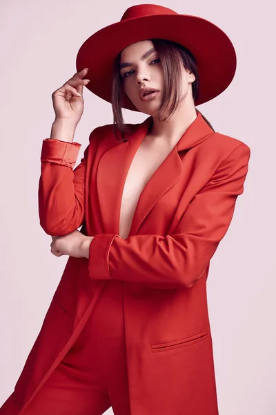 赤のファッショナブルなスーツとスタジオで白い背景に分離された広い帽子でエレガントな美しい女性の肖像画 — ストック写真