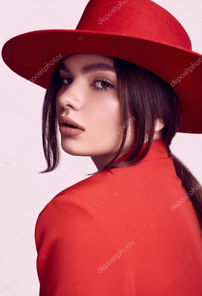 Portrait of elegant beautiful woman in a red fashionable suit and wide hat isolated on white background in studio