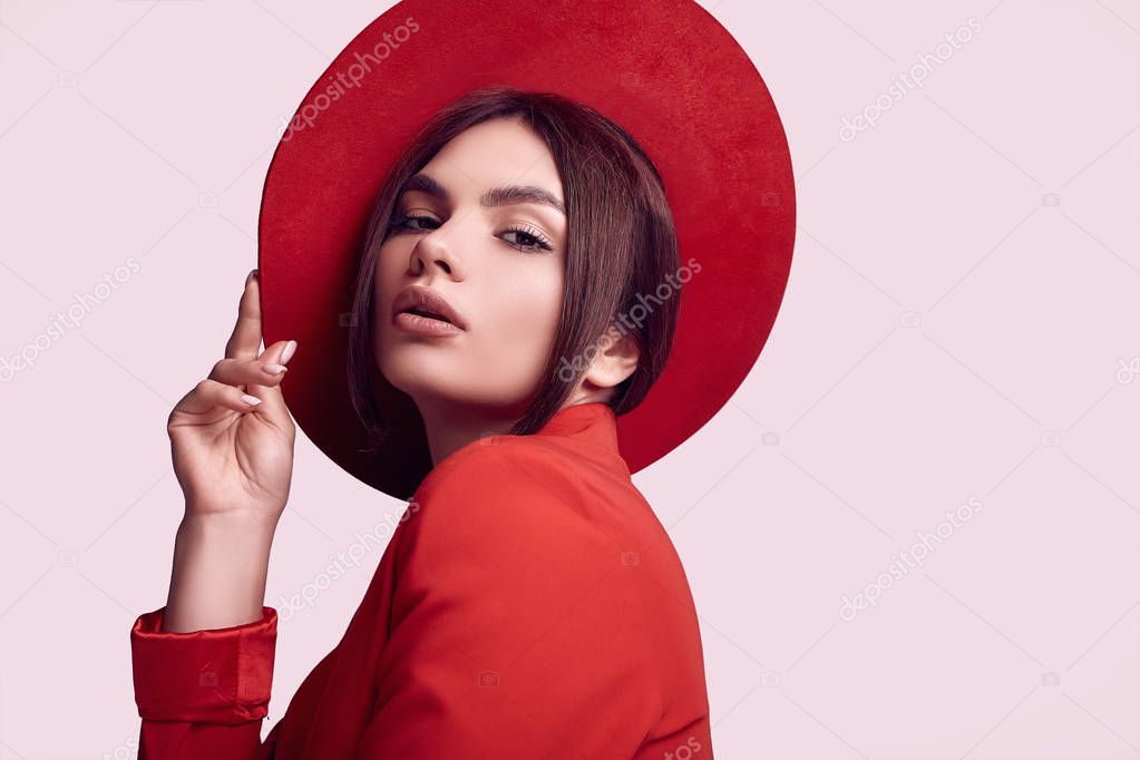 Portrait of elegant beautiful woman in a red fashionable suit and wide hat isolated on white background in studio