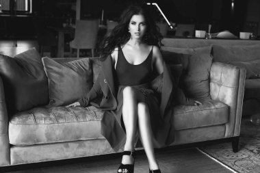 Muhteşem seksi esmer modeli moda elbiseli oturma odasında kanepede rahatlatıcı portresi. İç ateş.