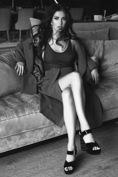 Portrait of gorgeous sensual brunette model in fashion suit relaxing on couch in living room. Interior shoot.