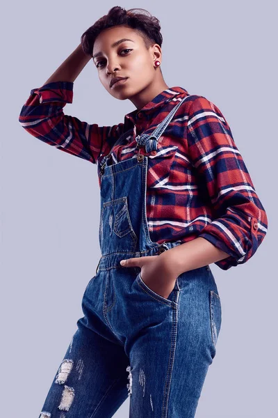 Studio のカラフルな背景にポーズ格子縞のシャツとデニムつなぎでショートヘアのグラマー エレガントな黒内気な少女の官能的な肖像画 — ストック写真