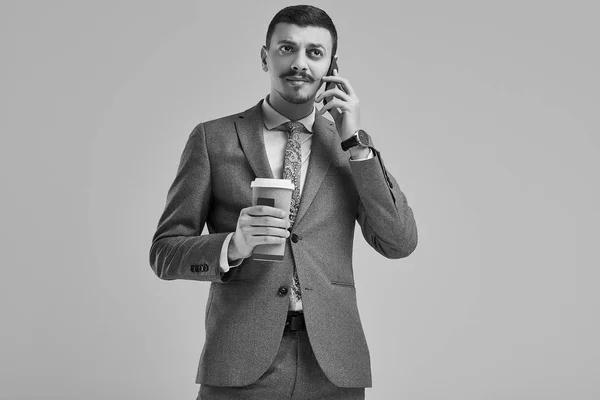 英俊的年轻自信的阿拉伯商人的肖像与花哨的胡子在时尚灰色的全套西装举行一杯咖啡和电话交谈 — 图库照片