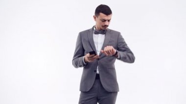 Yakışıklı genç emin Arapça işadamı beyaz stüdyo arka plan üzerinde izole bir telefon tutarak moda gri elbiseli süslü bıyıklı portresi