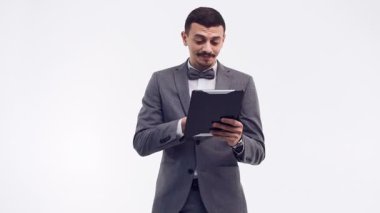 Yakışıklı genç emin Arapça işadamı beyaz stüdyo arka plan üzerinde izole tablet tutan moda gri elbiseli süslü bıyıklı portresi