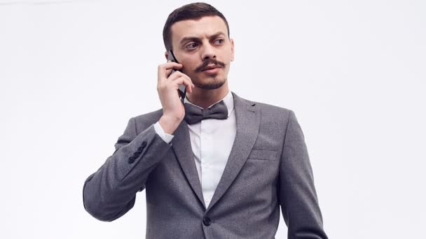 灰色スーツ白スタジオの背景に分離された携帯電話を保持で派手な口髭のハンサムな若い自信アラビア語ビジネスマンの肖像画 — ストック動画