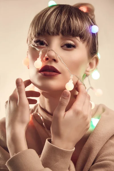 Fashion bright positive portrait of beautiful blond woman with christmas lights on the head. Studio shoot.