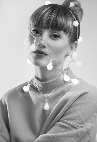 Fashion bright positive portrait of beautiful blond woman with christmas lights on the head. Studio shoot.