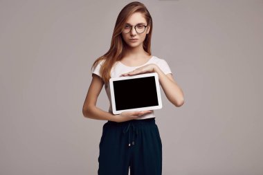 Beyaz gömlek ve dijital tablet gri arka plan üzerinde tutarak Gözlük Sevimli Genç kız portresi. Stüdyo çekimi.