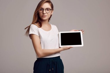 Beyaz gömlek ve dijital tablet gri arka plan üzerinde tutarak Gözlük Sevimli Genç kız portresi. Stüdyo çekimi.