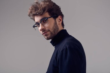 Moda portre Studio gri arka plan üzerinde siyah boğazlı kazak ve gözlük takıyor kıvırcık saçlı yakışıklı zarif biri