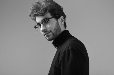 Moda portre Studio gri arka plan üzerinde siyah boğazlı kazak ve gözlük takıyor kıvırcık saçlı yakışıklı zarif biri