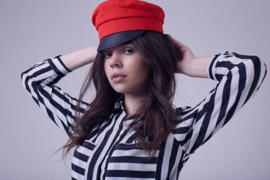 Bir şeritli bluz ve Studio beyaz arka plan üzerinde izole kırmızı şapka giyen moda esmer kadın portresi