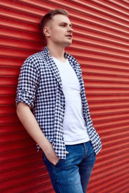 Kırmızı kapının yanında tişörtlü ve kot pantolonlu genç yakışıklı adam.