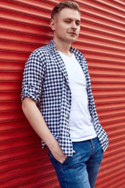 Kırmızı kapının yanında tişörtlü ve kot pantolonlu genç yakışıklı adam.