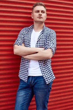 Kırmızı kapının yanında tişörtlü ve kot pantolonlu genç yakışıklı adam.