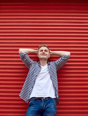 Kırmızı kapının yanında tişörtlü ve kot pantolonlu genç yakışıklı adam.