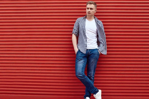 Joven hombre guapo en una camisa y jeans cerca de la puerta roja — Foto de Stock