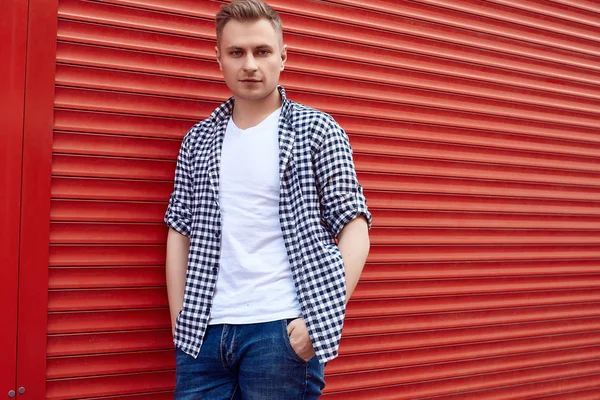 Joven hombre guapo en una camisa y jeans cerca de la puerta roja —  Fotos de Stock