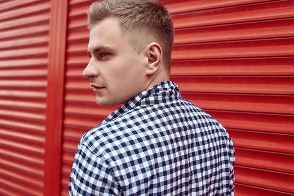 Joven hombre guapo en una camisa y jeans cerca de la puerta roja —  Fotos de Stock