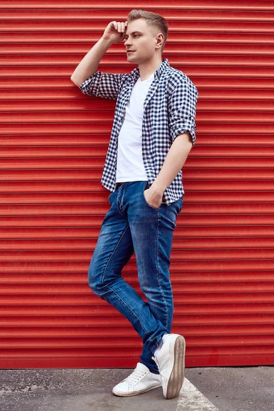 Joven hombre guapo en una camisa y jeans cerca de la puerta roja —  Fotos de Stock