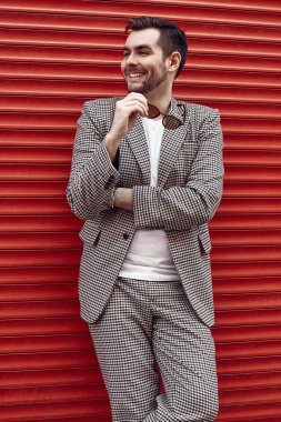 Kırmızı kapının yanında takım elbiseli, yakışıklı, vahşi bir adam.