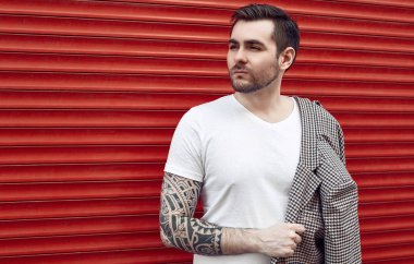 Kırmızı kapının yanında takım elbiseli, yakışıklı, vahşi bir adam.