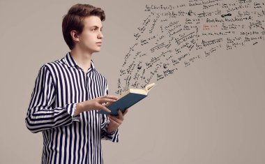 Çizgili gömlekli genç adam gri arka plan üzerine bir kitap okuyor.