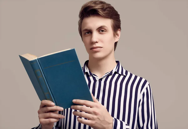 穿着条纹衬衫的年轻英俊男子正在阅读一本灰色背景的书 — 图库照片