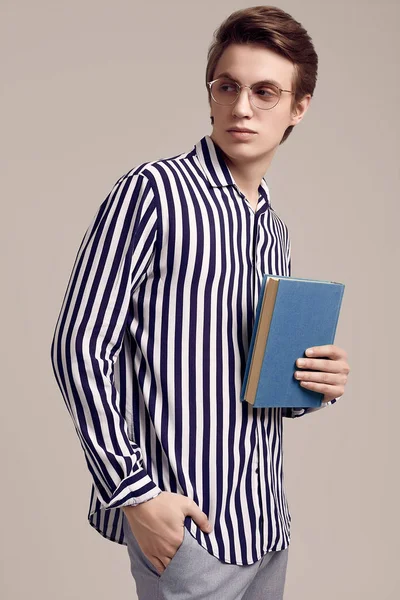 Молодий чоловік у смугастій сорочці позує з книгою на сірому фоні — стокове фото