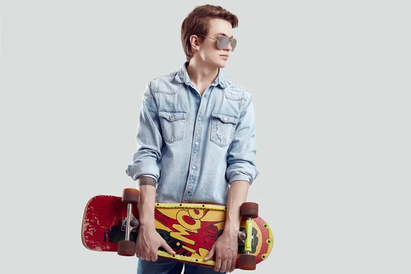 Хіпстер в сонцезахисних окулярах і джинсах позує зі скейтбордом — стокове фото