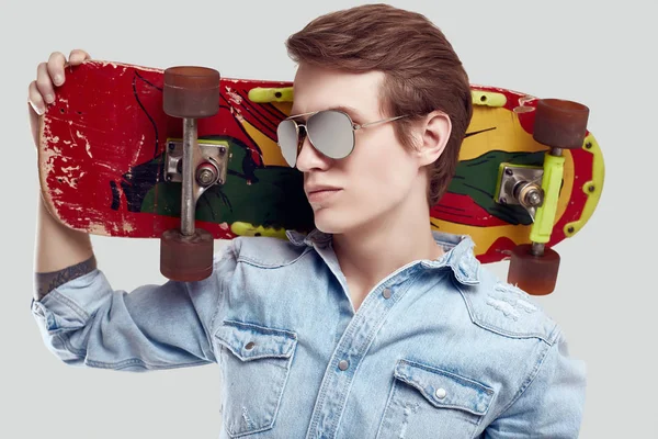Uomo hipster in occhiali da sole e giacca jeans in posa con skateboard — Foto Stock