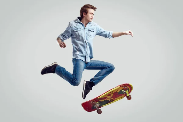 Bello hipster uomo in giacca jeans facendo il flip su skateboard alla moda — Foto Stock