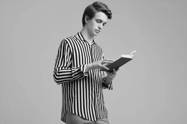 Fiatal jóképű férfi csíkos ing olvasó egy könyvet a szürke backg — Stock Fotó