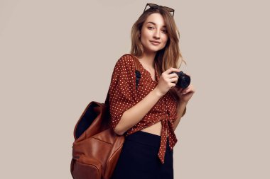 Sırt çantası ve fotoğraf makinesiyle gezmeye hazır güzel bir kadının portresi. Gülümseyen öğrenci kız tatile çıkıyor. Gri arkaplanda izole.