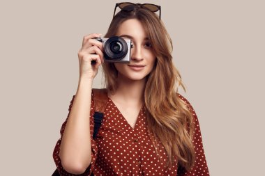 Sırt çantası ve fotoğraf makinesiyle gezmeye hazır güzel bir kadının portresi. Gülümseyen öğrenci kız tatile çıkıyor. Gri arkaplanda izole.