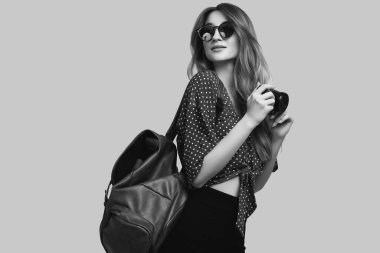 Sırt çantası ve fotoğraf makinesiyle gezmeye hazır güzel bir kadının portresi. Gülümseyen öğrenci kız tatile çıkıyor. Gri arkaplanda izole.