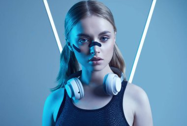 Beyaz kulaklıklı güzel sarışın kızın canlı renkli portresi stüdyoda neon ışıklarla müzik dinliyor.