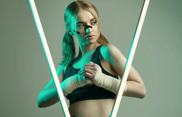 Vivid portrait of strong beautiful girl with blonde hair, sports figure, confident look and fists in protective boxing bandages posing on colorful neon light background