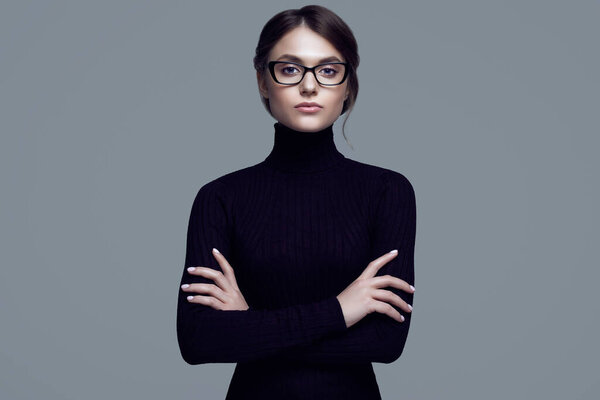 Portrait of cute student girl wearing black turtleneck sweater and stylish eyeglasses posing on gray background in studio