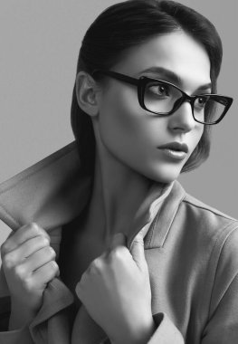 Stüdyoda koyu gri arka planda poz veren şık ceketli ve gözlüklü güzel hippi kadın portresi.