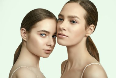 Açık tenli ve kusursuz makyajlı iki esmer kızın stüdyo portresi.