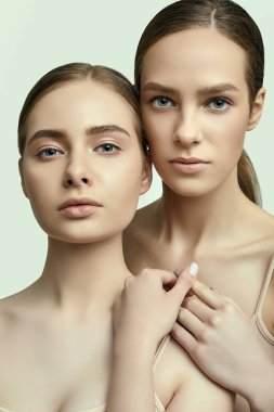 Açık tenli ve kusursuz makyajlı iki esmer kızın stüdyo portresi.