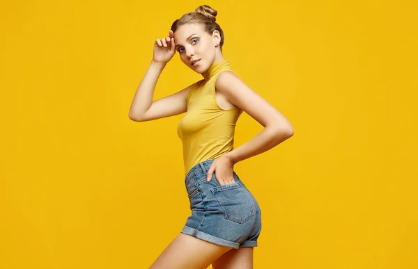 Positive portrait of gorgeous blonde hipster woman model with curly hair posing on colorful yellow background in studio
