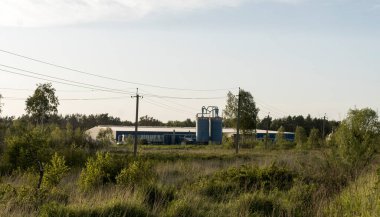 Ormanın yakınındaki tarlada fabrika. İki büyük tank ve dumanın geldiği bir pipo..