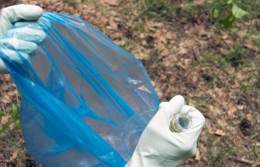İnsan doğadaki çöpleri temizler. Eldivenli eller çöp torbasına plastik bir şişe koydu. Birinci şahıs görünümü.