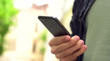 Kafkas asıllı, genç bir erkeğin eli ve telefonu yakın çekim. Adamın biri şehir caddesinde bir mesaj yazıyor.