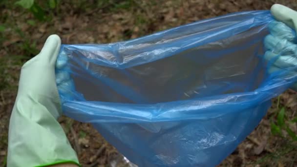 一个戴手套的年轻人的手把一个塑料瓶放进垃圾袋里 森林中的垃圾收集 — 图库视频影像