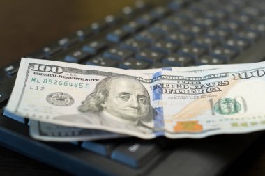 Yüz dolarlık banknotlar siyah bir bilgisayar klavyesinde yatıyor. Serbest çalışan konsepti için maaş. Kapat..